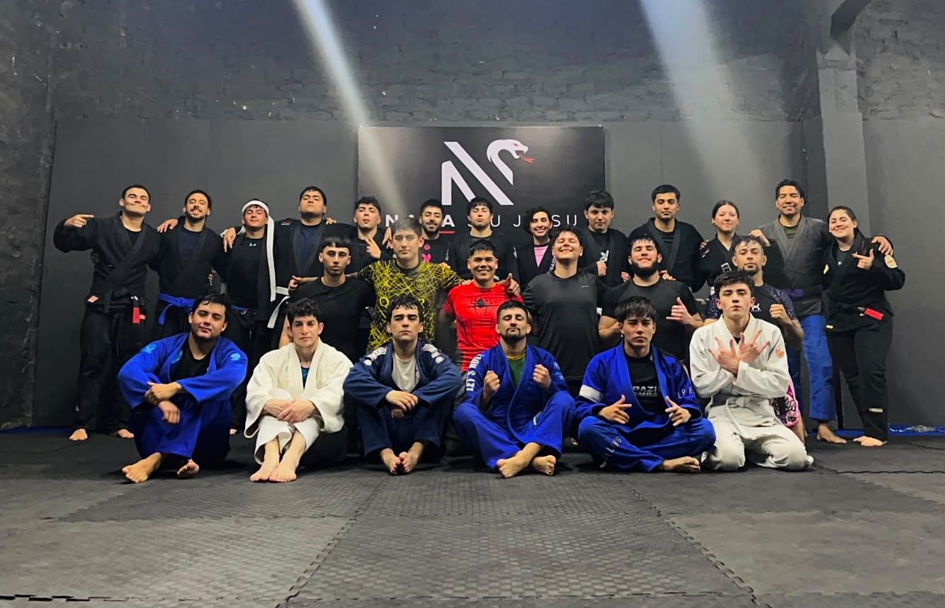 Grupo de entrenamiento de Naga reunido en el tatami con el letrero de la academia al fondo