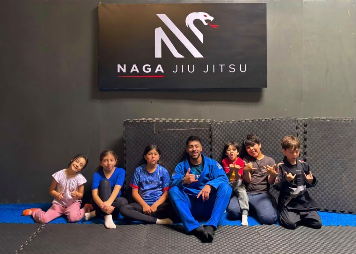 Grupo Kids sentado en el tatami bajo el letrero de Naga Jiu Jitsu